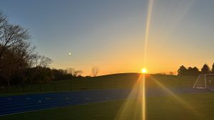 Sunset behind a hill with a black fence, blue track, and white soccer goal in the foreground (Woodridge, Illinois)
