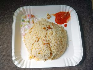 Rice served with salads and pickle on a white disposable plate. 