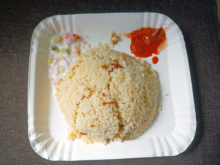 Rice served with salads and pickle on a white disposable plate.