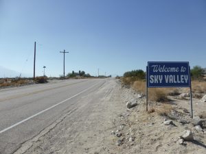 A paved road and blue sky with a sign welcoming you to Sky Valley, California