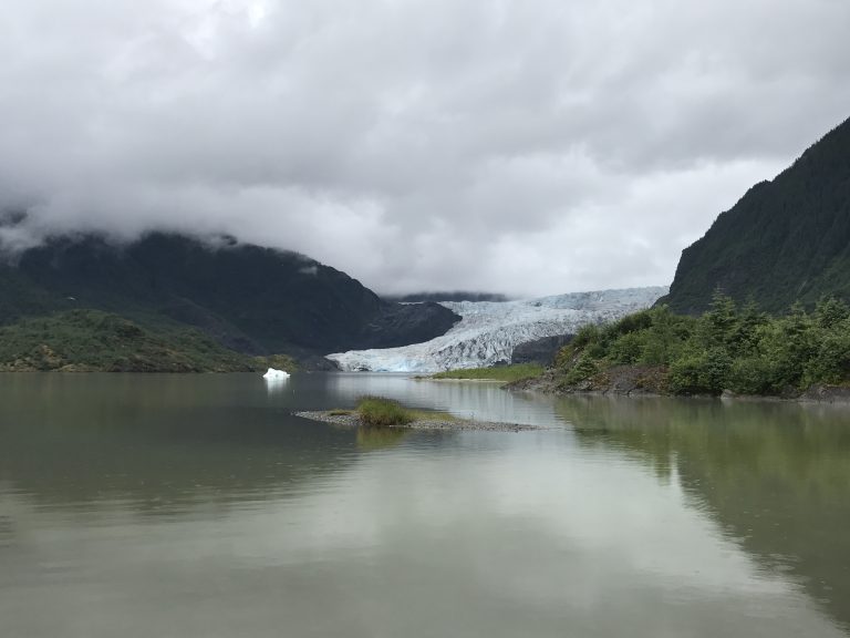 A view of the Mendenhall Glacier from the viewing are at the Mendenhall Glacier Visitor Center in Juneau, Alaska in July of 2017. The surrounding area is green with the glacier sticking out into the Mendenhall Lake.