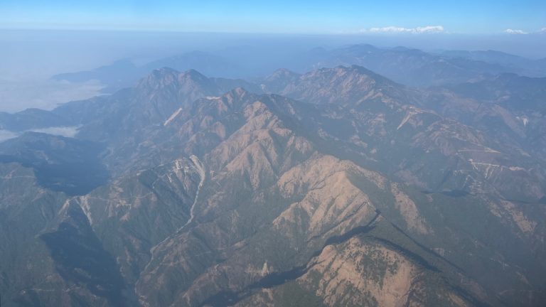 Ariel view of a mountain range with a distant view of snow-capped mountains.