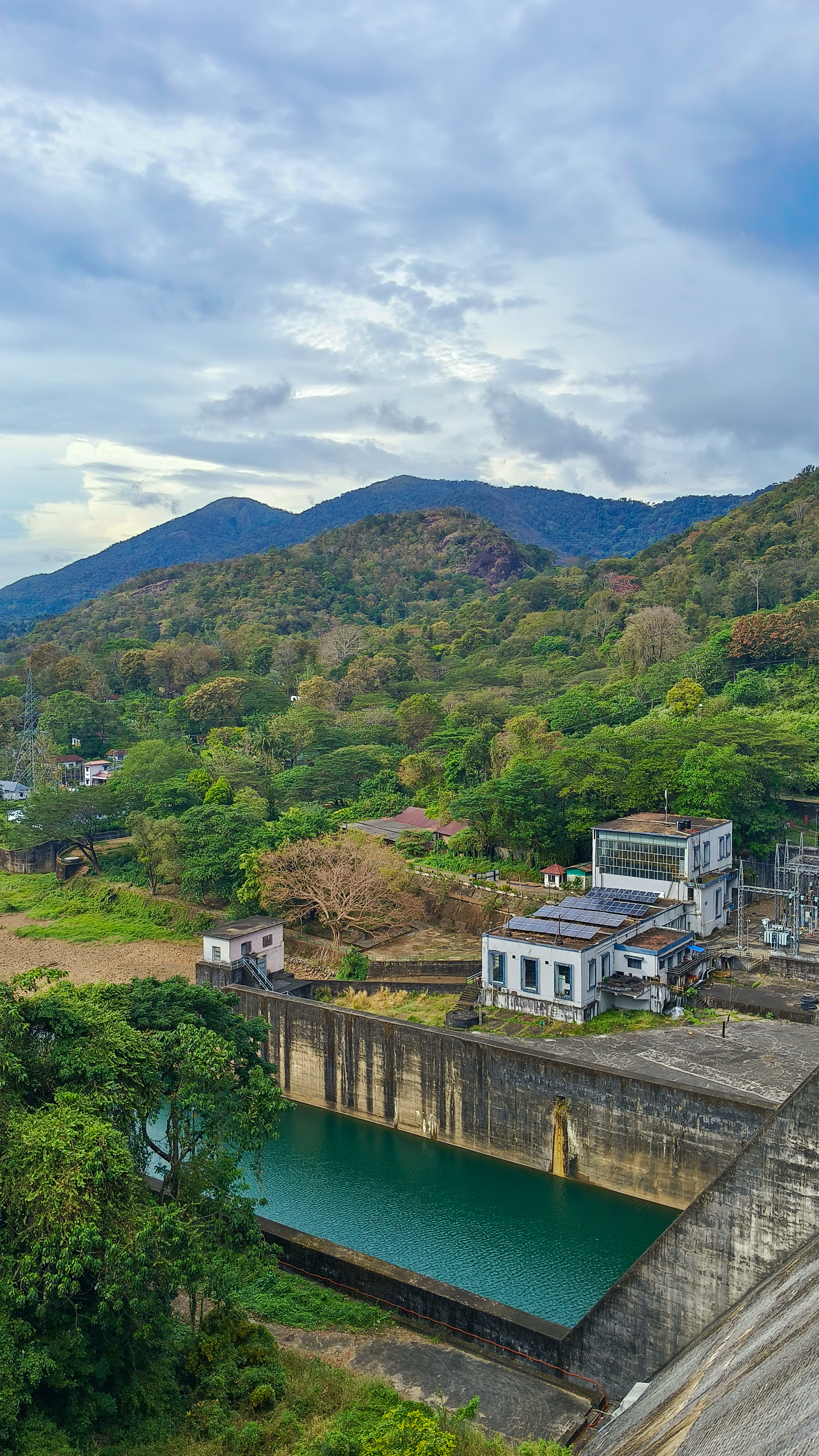 A picturesque scene unfolds at Thenmala Dam, where lush greenery, majestic mountains, and the gentle flow of water from the dam create a captivating view.