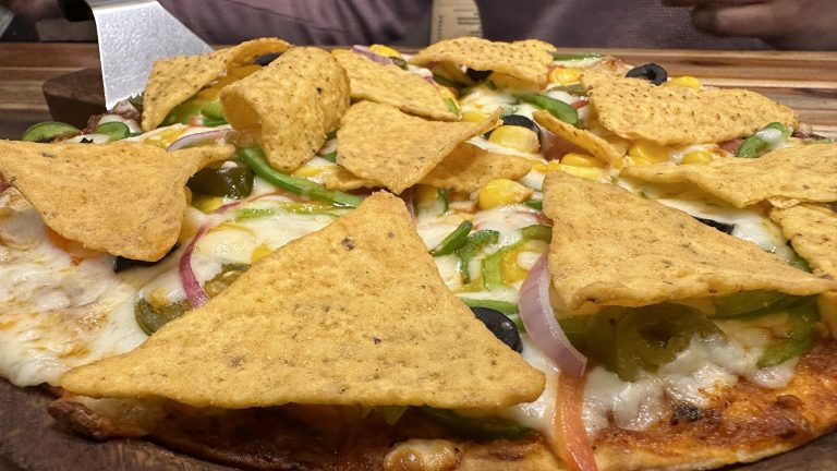 Nachos spread over a pizza served on wooden plate.