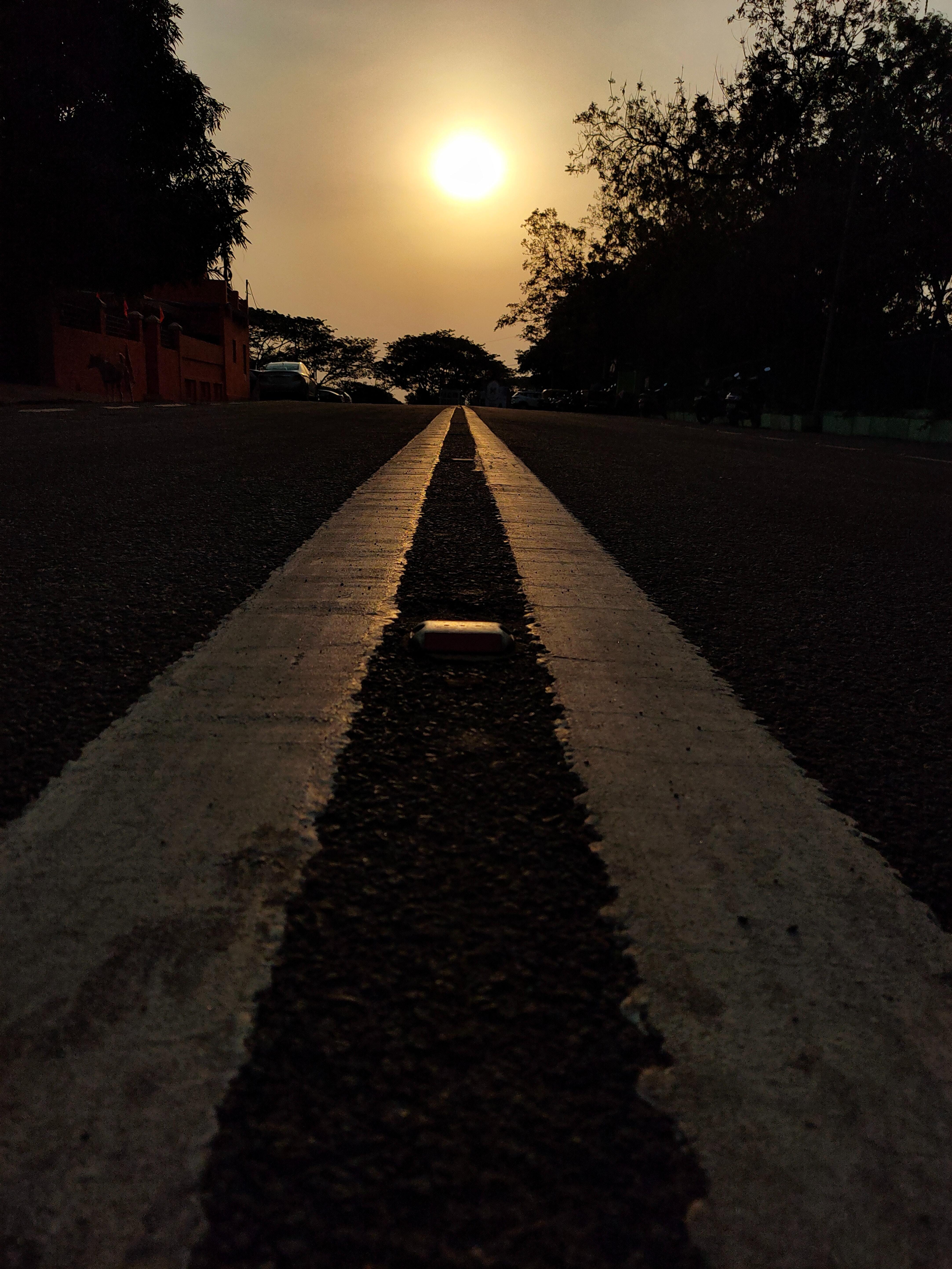 Looking down the stripes in the center of a road as the sun sets in the distance.