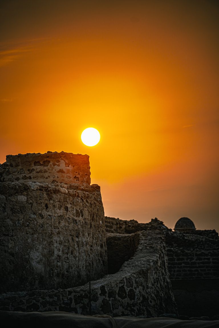 Enchanting sunset at Bahrain Fort: Silhouetted against the ancient stronghold, the sky transforms into a canvas of warm hues, casting a serene glow over the historical landscape, capturing the essence of timeless beauty and tranquility.