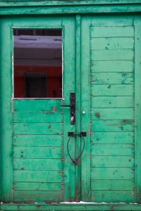 Old green wooden door with a window and a lock.