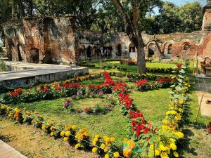 Flower garden with various different color flowers including yellow, orange, red and pink, in front of a historical building.