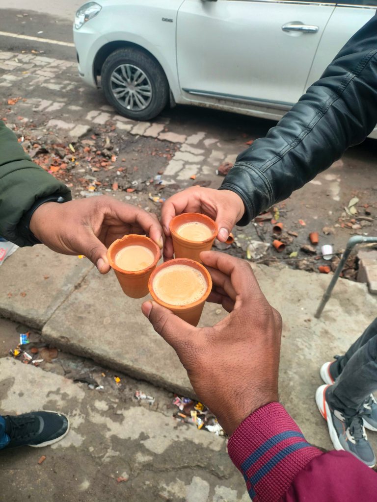 Three hands holding cups of chai. There is a white car in the background.