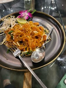 A Thai cuisine called Pad Thai served on a dish accompanied by a slice of lemon and utensils.