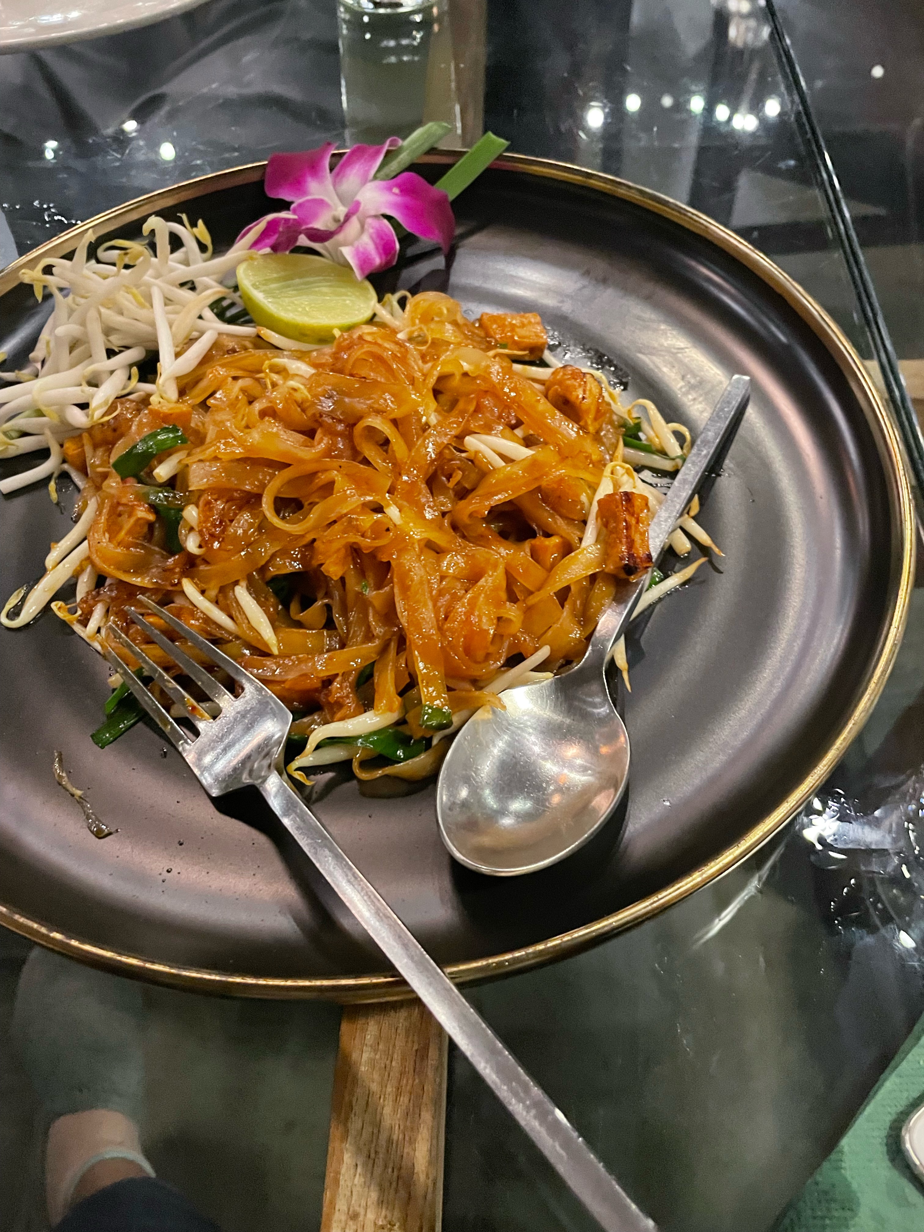 A Thai cuisine called Pad Thai served on a dish accompanied by a slice of lemon and utensils.