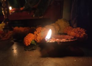 A captivating photo of a lit oil lamp (diya) casting a warm yellow flame, surrounded by vibrant flowers, creating a serene and enchanting scene during the festival.