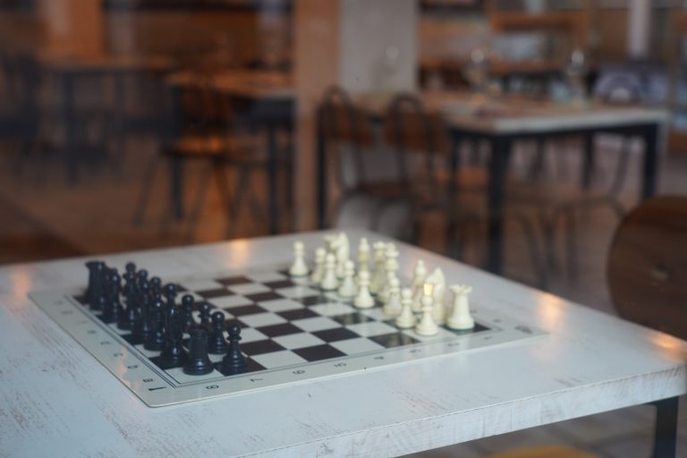 Chess board set to play on a white wooden table inside a café.