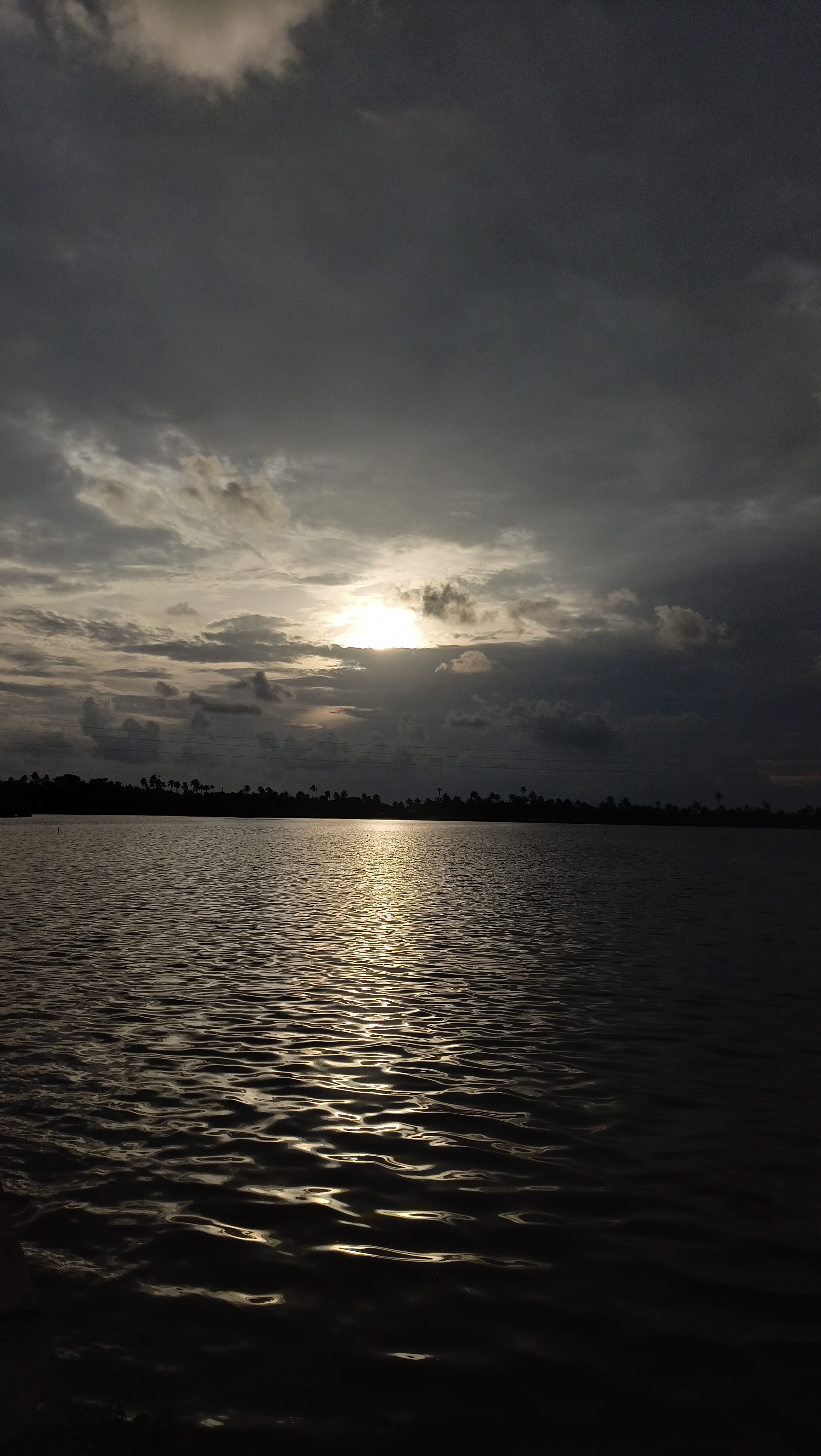 A blueish black sky, with the sunrays hiding behind clouds and reflection in the lake.