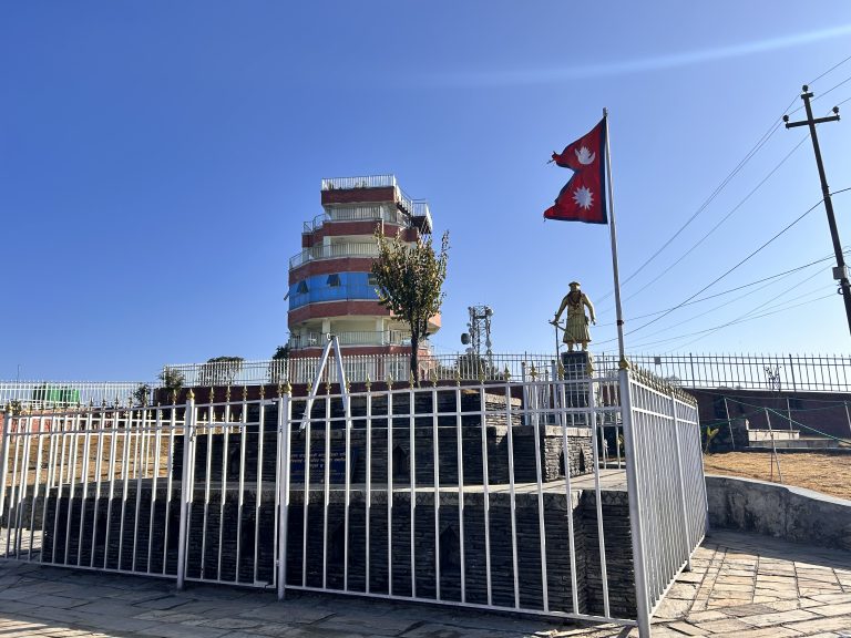 A scene capturing a tower, statue, and the waving flag of Nepal in the foreground.