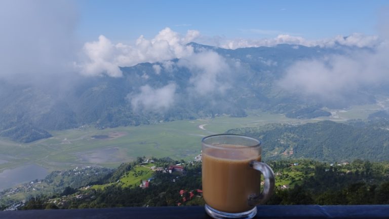 A cup of tea on a rail, with a view of the valley and mountains covered with cloud in the background.