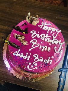 A pink violet cake with a white birthday message. 