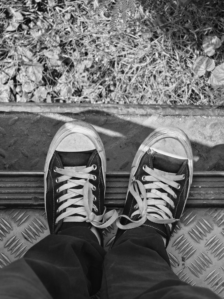 Tennis shoes standing on a step with grass just below the step.