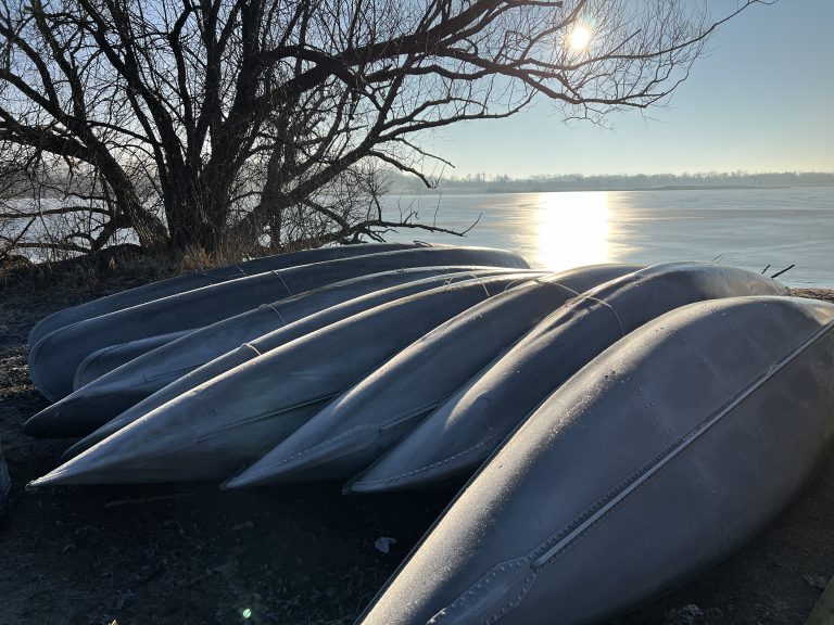 Canoes stacked side-by-side on a lake beach at sunrise (Fish Lake, YMCA Camp Duncan, Ingleside, Illinois)