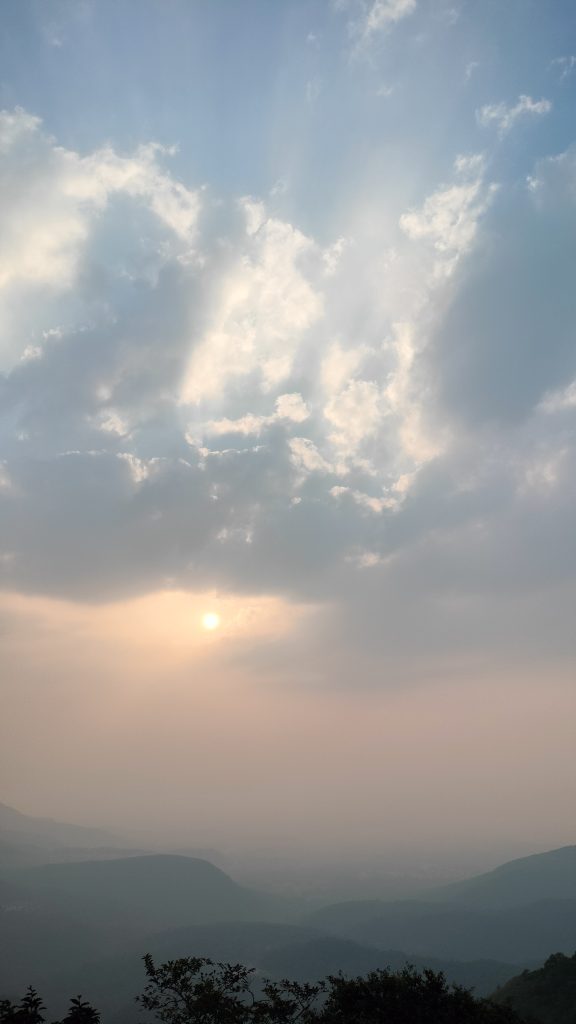 A captivating moment captured at fonda ghat, as the sun begins to dip behind the hills, casting a warm glow across the sky, yet half of the sky retains the vibrant colors of daytime.
