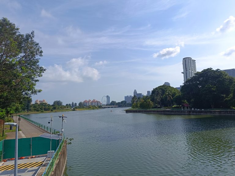 A serene lake with calm waters in Singapore with a picturesque bridge and nice building structures shining with sunlight.