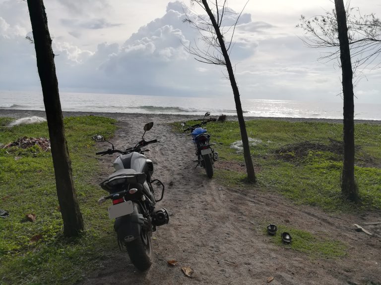 Two motorcycles parked on the beach with clouds and sea in front.