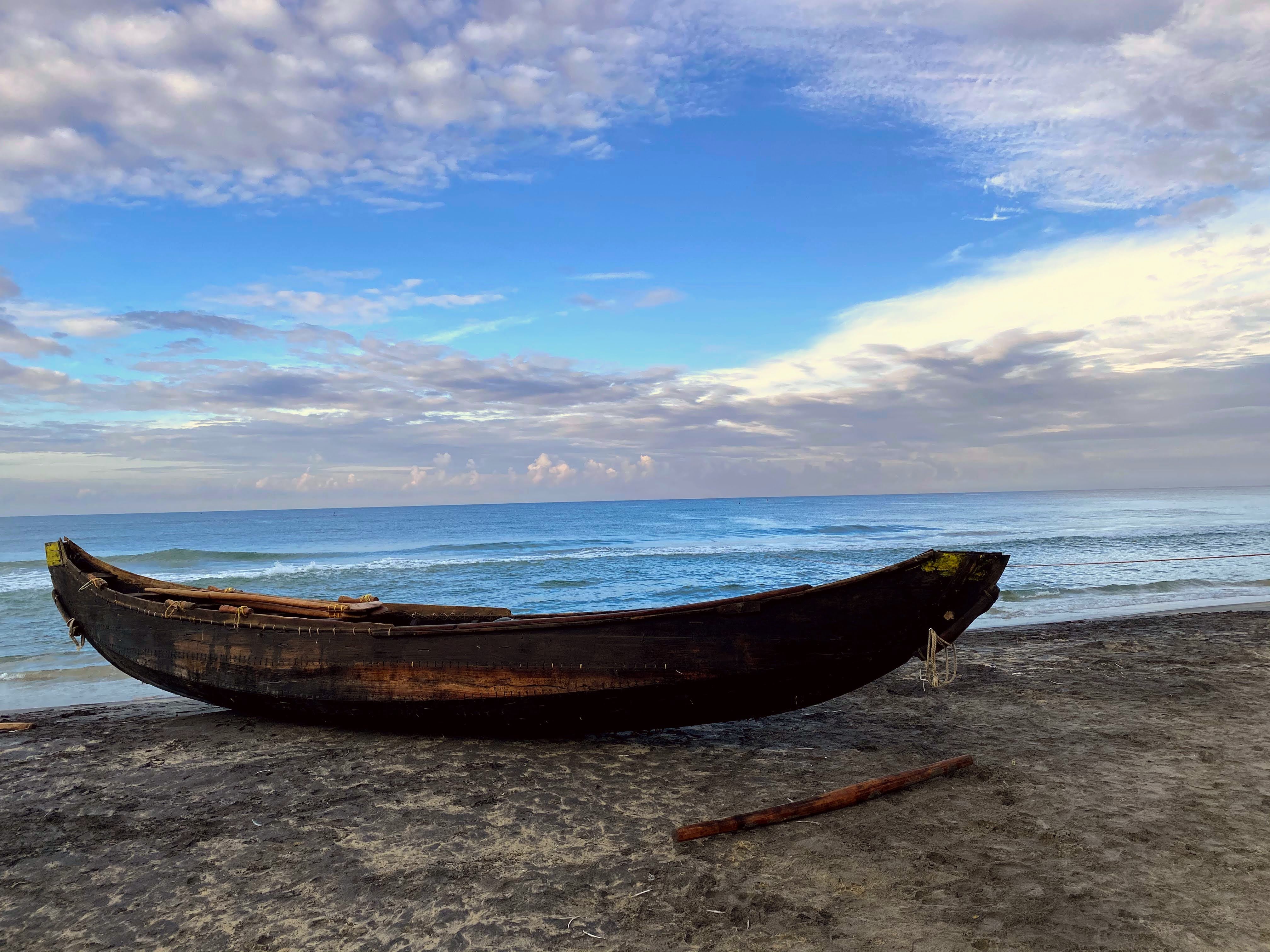   A boat lies on a sandy beach, amidst tranquil waves and a cloudy blue sky.