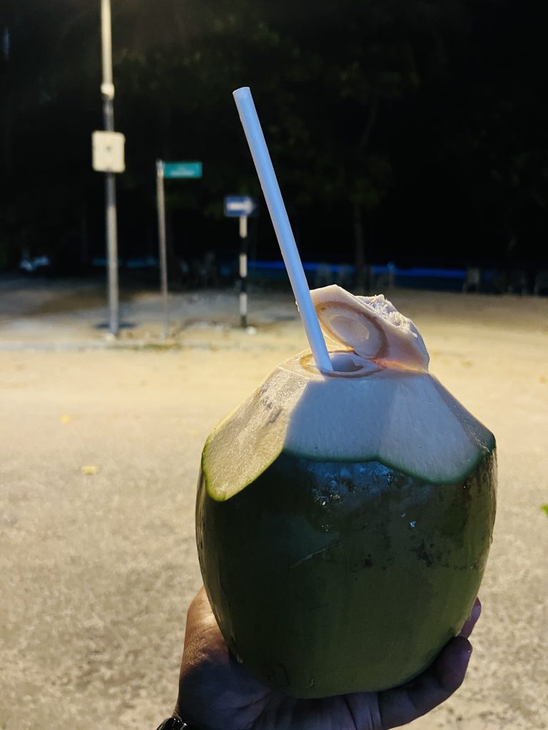 A man holding a coconut in his hand which is ready to drink using a straw.