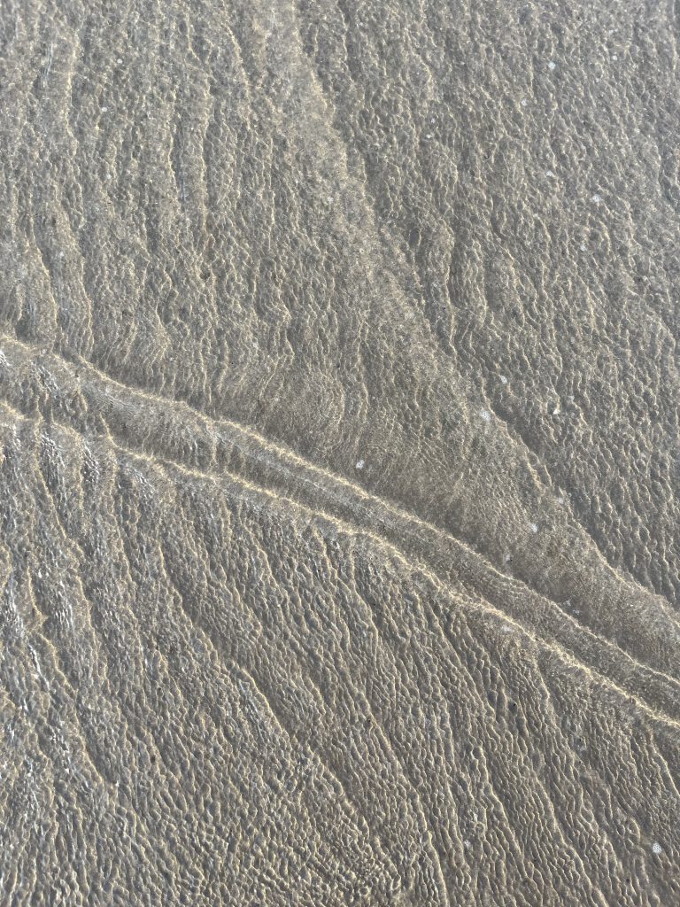 A top view of the water waves gently rolling over the sandy texture of a summer beach.