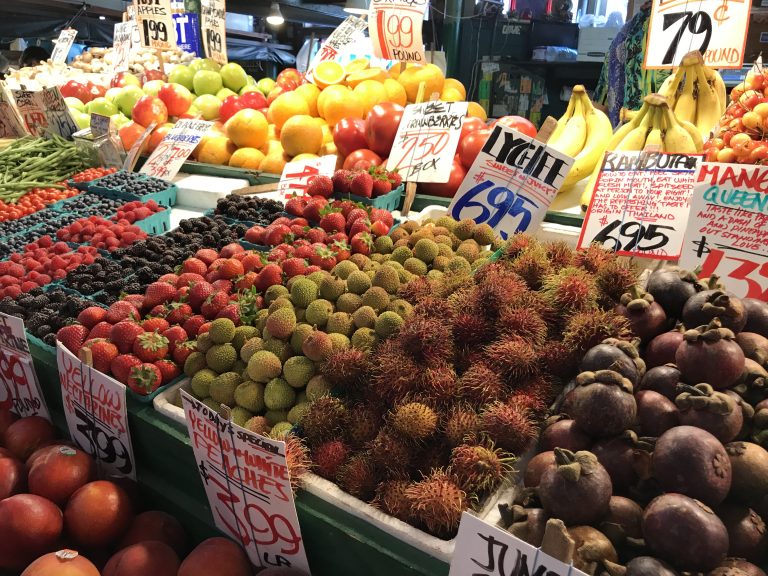 A colorful fruit stand inside Pike Place Market in Seattle, Washington featuring various berry and apple varieties, bananas, nectarines, and rambutan.