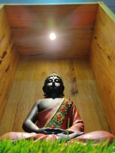 Budha statue in a wooden shelfs with a light on the roof.