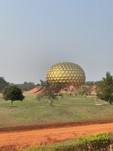 Matrimandir a golden sphere structure constructed from circle and triangle shapes, edged with brick slopes in Auroville, Pondicherry stands in a grass park dotted with trees. 