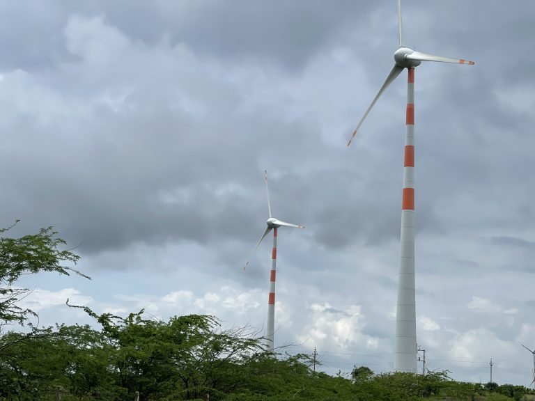 White and orange wind turbines rise above the trees into a cloudy sky