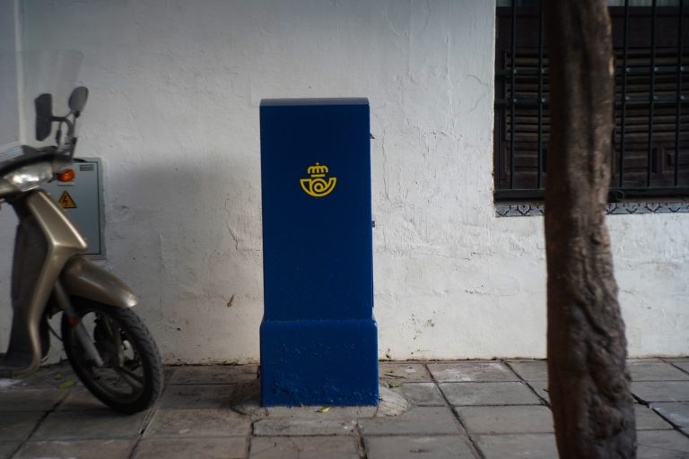 Square deep blue mailbox in the street under a tree