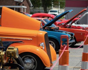Car show with orange, blue and red hot rods in the foreground with their hoods popped, separated by traffic cones. Fayetteville, New River Gorge National Park, Fayette County, West Virginia