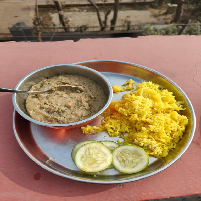 Fried rice, sauce and seeded cucumber with served in circular metal dishes, laying on a painted wall, a spoon ready for use resting in the sauce.