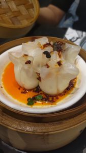 A New York cheese and chili?oil: Dim sum packed with creme cheese, button mushrooms, water chestnut and topped?with?chili?oil, served on a white ceramic bowl. 