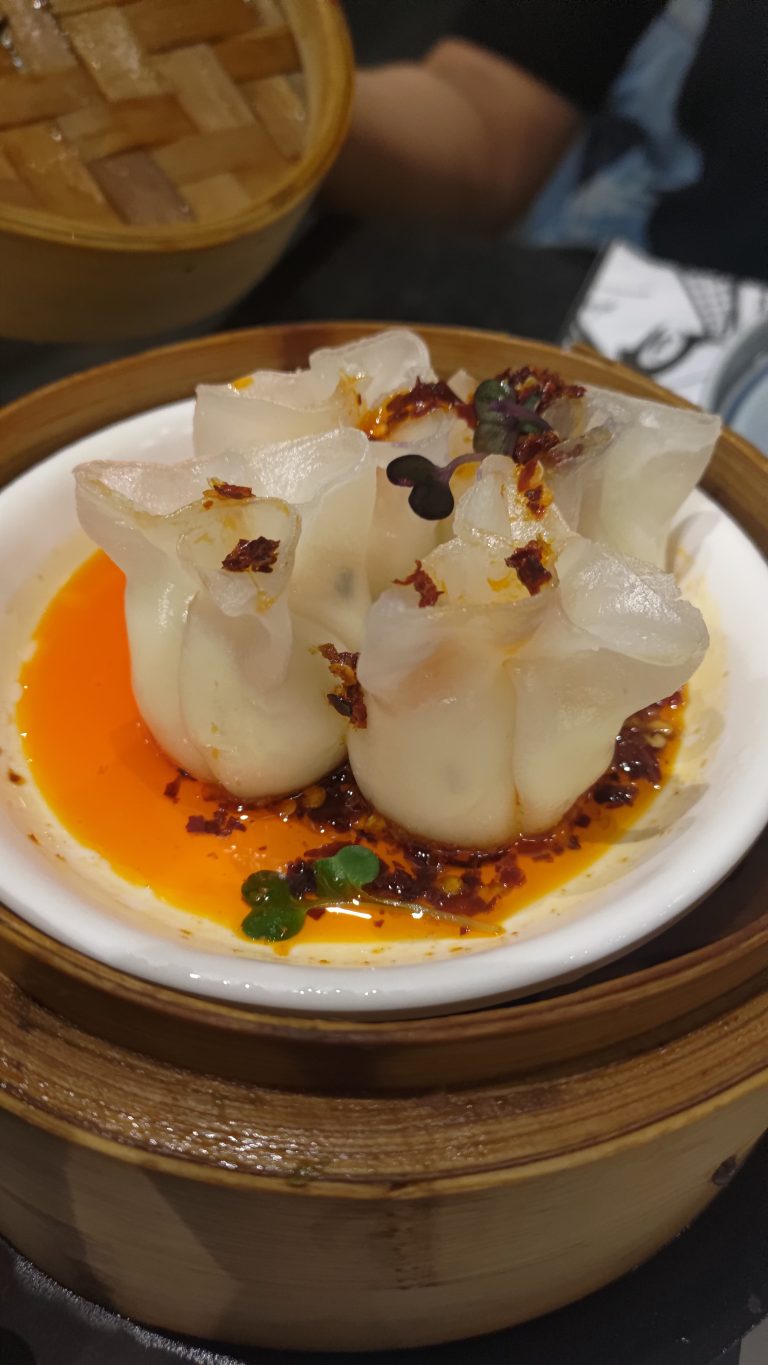 A New York cheese and chili?oil: Dim sum packed with creme cheese, button mushrooms, water chestnut and topped?with?chili?oil, served on a white ceramic bowl.