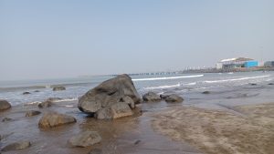 A massive rock rests on the sandy beach, close to the water's edge, creating a picturesque scene.