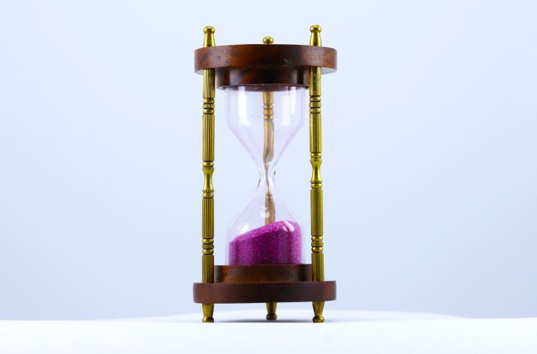 An hourglass with wooden top and bottom and gold metal structure with dark pink sand inside.