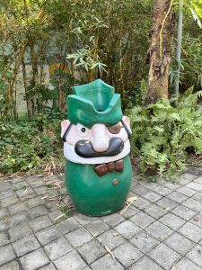 A green colored Mario themed trashcan on the side of a walkway. 
