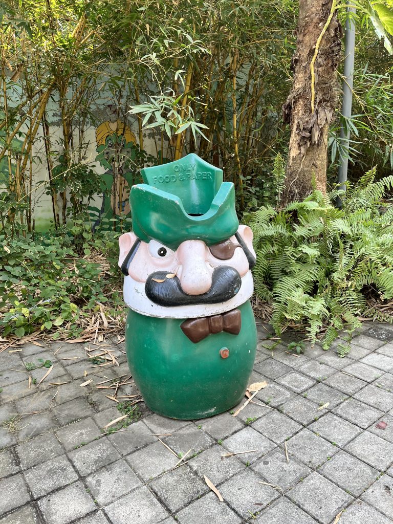 A green colored Mario themed trashcan on the side of a walkway.