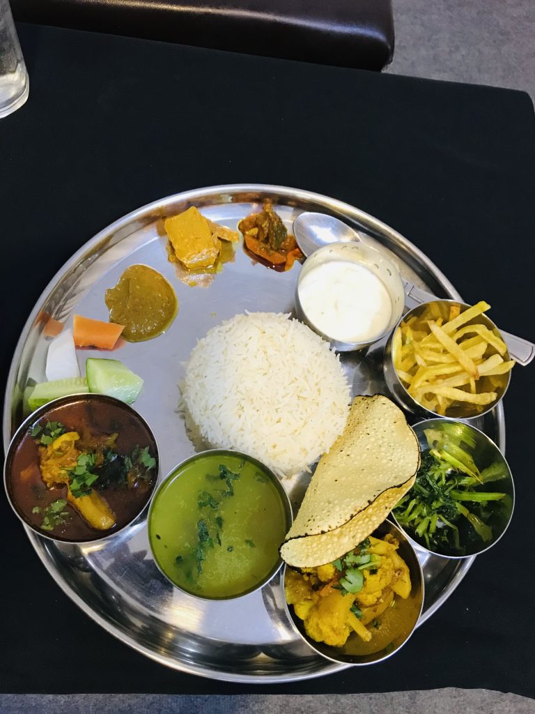 A flawless array of Thakali cuisine is served on a silver-toned plate.