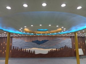 Round ceiling with lights over a mural of trees and mountains made from wood
