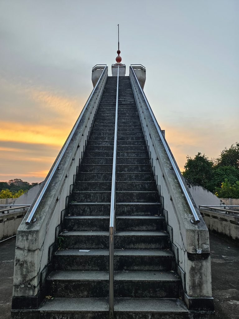 Steps lead to the top of a viewpoint with rails through the middle and sides, against the golden rays of the evening sky in the background in Peechi, Thrissur, Kerala.