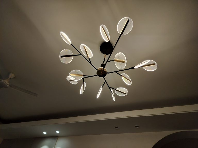 A modern chandelier with multiple illuminated oval elements attached to a central black sphere, mounted on a ceiling with soft ambient light.