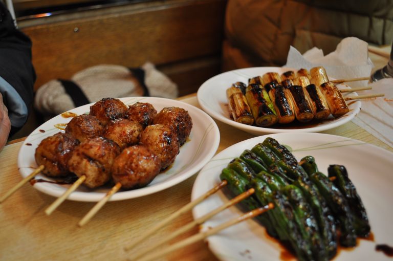 Tsukune (Japanese chicken meatball) skewer, shishito (Japanese pepper) skewer, long onion skewer at a yakitori bar in Tokyo, Japan.