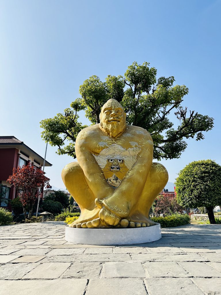 A Yellow Statue of a very burly man.  The statue is probably 20 feet/6 meters tall.  There’s a demon face painted on its chest.