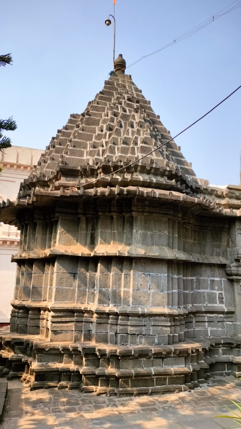 1300 year historical Shiva Temple, Siddhagiri math, Kanerimath, Kolhapur with a stepped pyramidal tower structure, adorned with geometric patterns, under a clear sky.