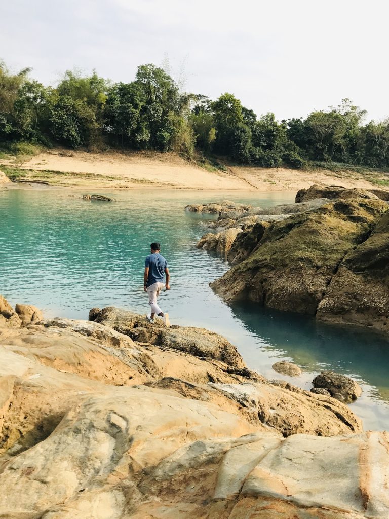 a boy is walking beside blue river photography